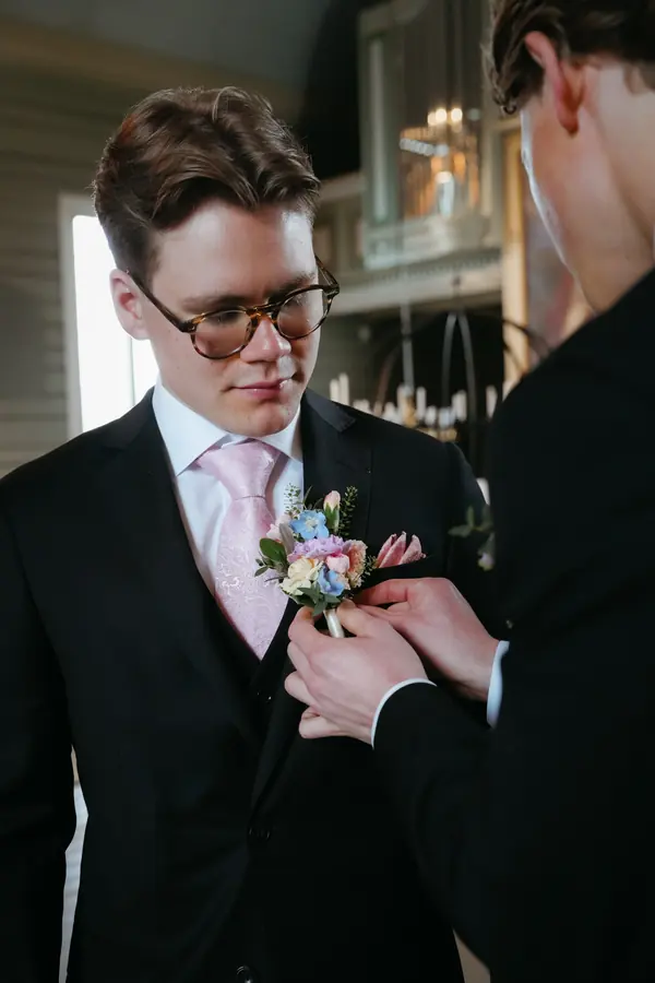 Forlover fester blomster på brudgommens jakkeslag.