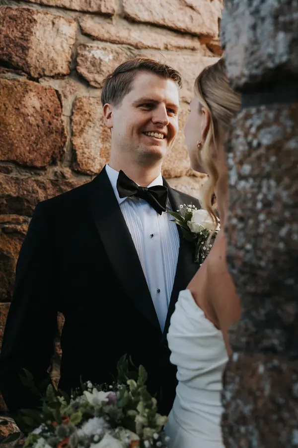Brudepar står tett sammen ved en rustikk steinvegg.